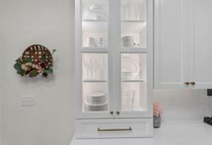 A beautiful backlit white built in kitchen cabinet filled with dishes.