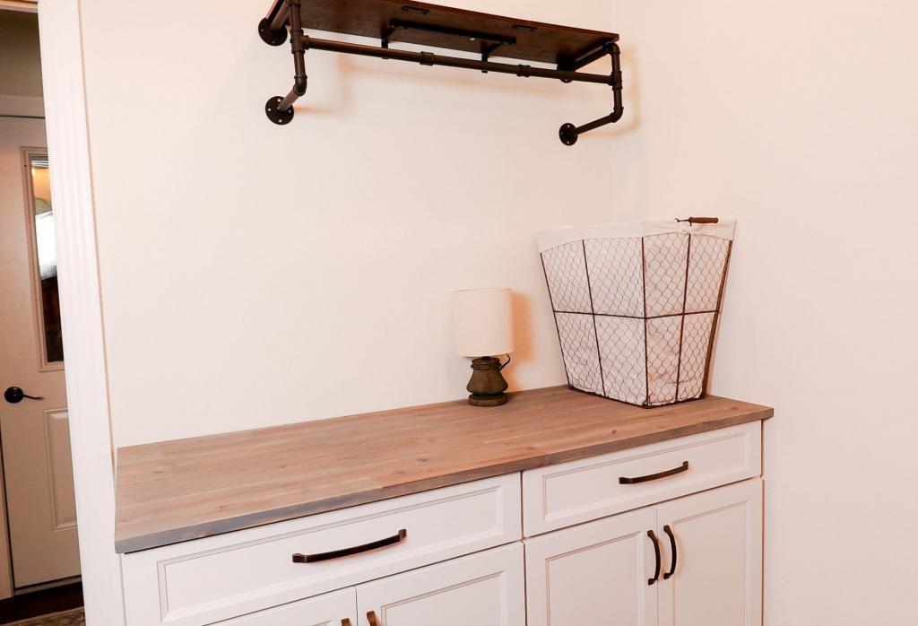 Rustic laundry room with natural wood counter tops and Ivory Koch Cabinets and iron shelf.