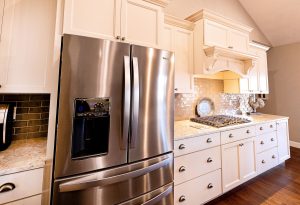 A modern kitchen with white cabinets, a stainless steel French door refrigerator with a water dispenser, a gas cooktop, marble countertops, and a metallic subway tile backsplash.